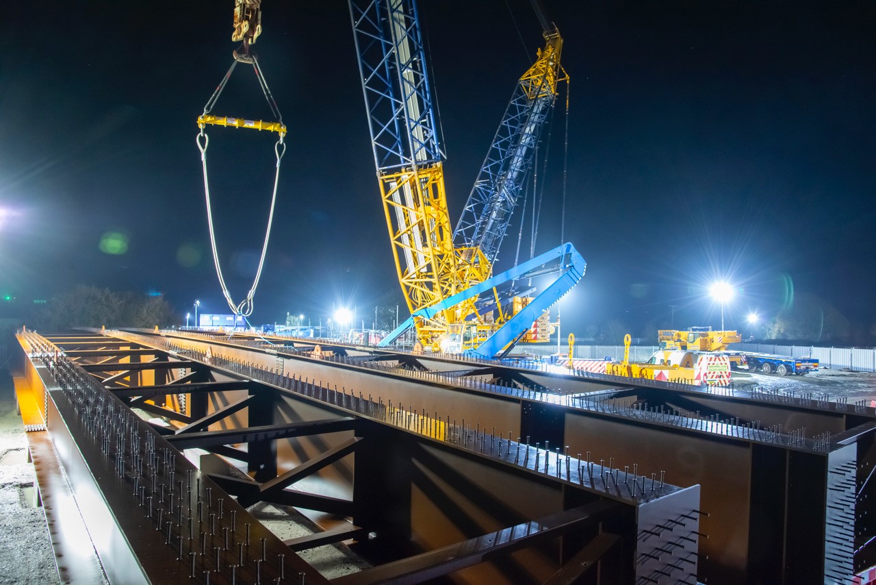 Crawler crane lifting steel bridge beams at night